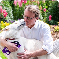 Martin Boney kissing his dog outside in front of flowers.